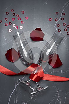 Top view of champagne glasses with a red ribbon, rose petals and small hearts