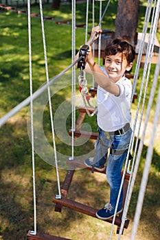 Top view of cheerful preteen boy climbing at rope park