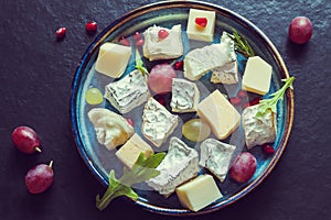 Top view cheese plate assortment of various types of cheese and grapes with pomegranate seeds dark background