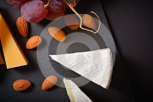 Top view of Cheese platter with hard and soft cheese pieces, grape, almonds on black slave stone board