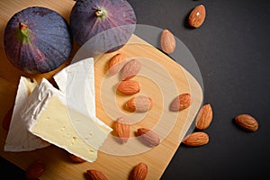 Top view of Cheese platter of Soft French Brie cheese cuts served with almond nuts and fig berries on wooden board