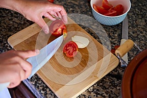 Top view of chef& x27;s hands using a kitchen knife, cutting fresh ripe organic tomatoes on a wooden board