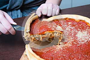 Top view of Chicago pizza. Woman hands cutting Chicago style deep dish italian cheese pizza with tomato sauce and beef meet inside