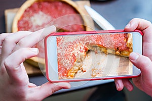 Top view of Chicago pizza. Woman hands taking photo with smart phone of Chicago style deep dish italian cheese pizza with tomato