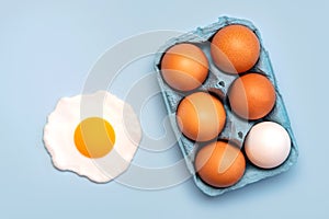 Top view of chicken eggs in an open blue cardboard box and a fried egg