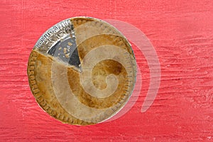 Top view of a chicken meat pie with one slice missing on a red painted tabletop