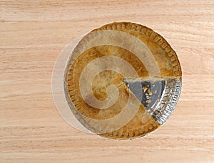 Top view of a chicken meat pie with one slice missing on a wood table