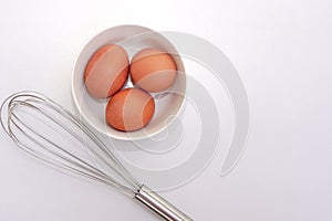 Top view of chickken eggs in a bowl and egg whisks on white background.