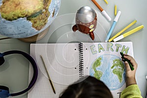 Top view of child girl draws planet earth with wax colors on school notebook for Earth day - Little activist girl writes the