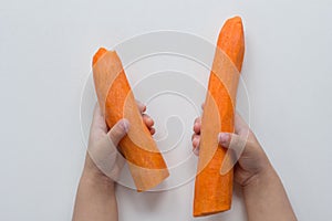 Top view of child hands holding two peeled carrots on the white background