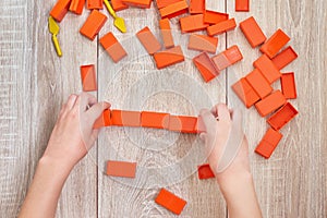 Top view of child hands playing with orange toy bricks. Concept of kids lerning and education. Baby leisure with developing toys