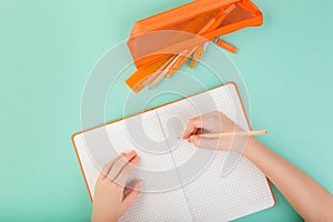 Top view of child hands writing in an empty notebook. Doing homework concept. Orange color.