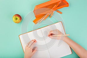 Top view of child hands writing in an empty notebook. Doing homework concept. Orange color.