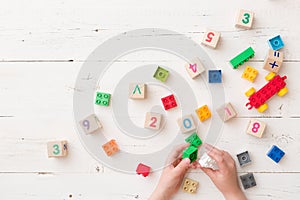 Top view on child`s hands playing with wooden cubes with numbers and colorful toy bricks on white wooden background