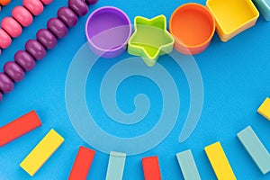 Top view children educational games, frame kids toys blue paper background. Multicolored wooden bricks, abacus, circles