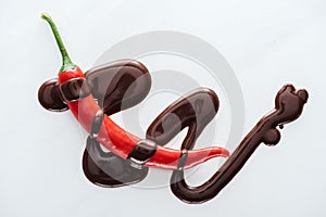 Top view chili with spilled melted dark chocolate on white background.