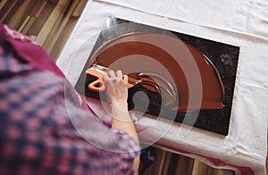 Top view of chocolatier holding cake scraber and cooling melted chocolate mass on a marble table