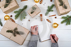 Top view of Christmas background with blank empty notebook and girl& x27;s hands with pen writing goals on white wooden.