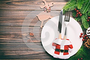 Top view of Christmas dinner on wooden background. Plate, utensil, fir tree and holiday decorations with copy space. New Year time