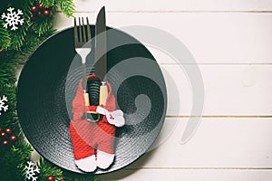 Top view of Christmas dinner on wooden background. Plate, utensil, fir tree and holiday decorations with copy space. New Year time