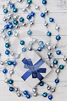 Top view Christmas gift with blue ribbon and silver and blue Christmas balls on white wooden background