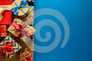 Top view on Christmas gifts wrapped in gift paper decorated with ribbon on blue paper background.