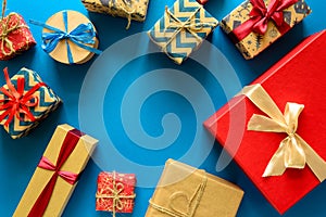 Top view on Christmas gifts wrapped in gift paper decorated with ribbon on blue paper background.