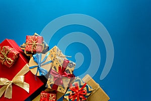 Top view on Christmas gifts wrapped in gift paper decorated with ribbon on blue paper background.