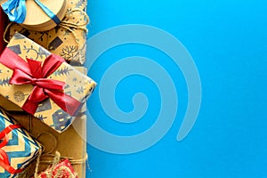 Top view on Christmas gifts wrapped in gift paper decorated with ribbon on blue paper background.