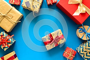 Top view on Christmas gifts wrapped in gift paper decorated with ribbon on blue paper background.