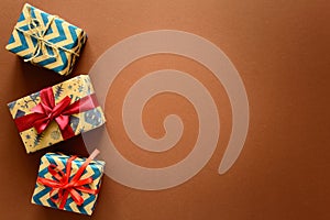 Top view on Christmas gifts wrapped in gift paper decorated with ribbon on brown paper background.
