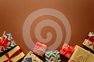 Top view on Christmas gifts wrapped in gift paper decorated with ribbon on brown paper background.