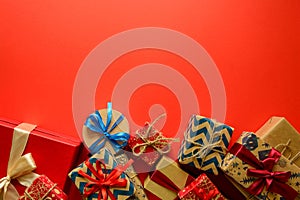 Top view on Christmas gifts wrapped in gift paper decorated with ribbon on red paper background.