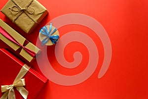 Top view on Christmas gifts wrapped in gift paper decorated with ribbon on red paper background.