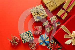 Top view on Christmas gifts wrapped in gift paper decorated with ribbon on red paper background.