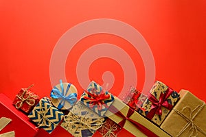 Top view on Christmas gifts wrapped in gift paper decorated with ribbon on red paper background.