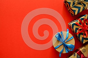 Top view on Christmas gifts wrapped in gift paper decorated with ribbon on red paper background.