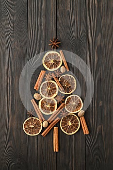 Top view of Christmas tree made from anise star, cinnamon sticks, orange dry, and nutmeg on a dark wooden background.