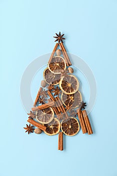 Top view of Christmas tree made from anise star, cinnamon sticks, orange dry, and nutmeg on pastel blue background.