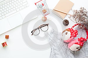 Top view of Christmas and winter shopping online concept on white desk. White laptop, shopping cart, gift boxes, notebook, eyeglas
