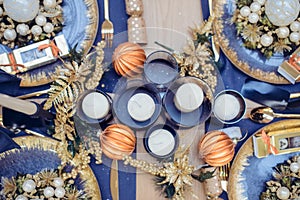 Top view Christmastime table setting, festive dinnerware decorated with details and candles in Blue and Gold colors. Navy Blue