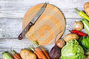 top view of circle cutting board, knife and fresh vegetables on wooden table top