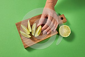 A woman`s hand takes a slice of organic fresh green lime on a wooden cutting board. Slices of lime on a board on a green