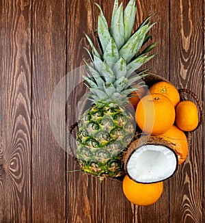 top view of citrus fruits as pineapple coconut orange tangerine in basket on wooden background with copy space