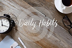Top view of clock,notebook,pen,glasses and coffee on wooden background written with Daily Habits