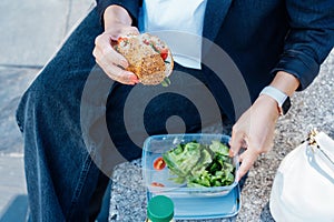 Top view close up business woman eating sandwich and fresh salad on lunch break sitting on bench at park. Balanced diet