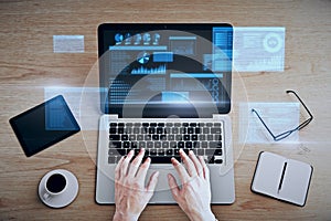 Top view and close up of businessman hands using laptop keyboard with glowing business chart hologram on screen at wooden desktop