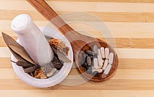 Top view Close-up  of different spices in white mortar pestle and a wooden spoon containing ayurvedic pills on a striped wood