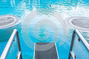 Top view close-up on a diving board against the background of a pool with blue water in which a person swims. The concept of summe