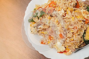 Top view, close up and focus on fried rice mixed with various vegetables and meats in white plate place on dark brown wooden